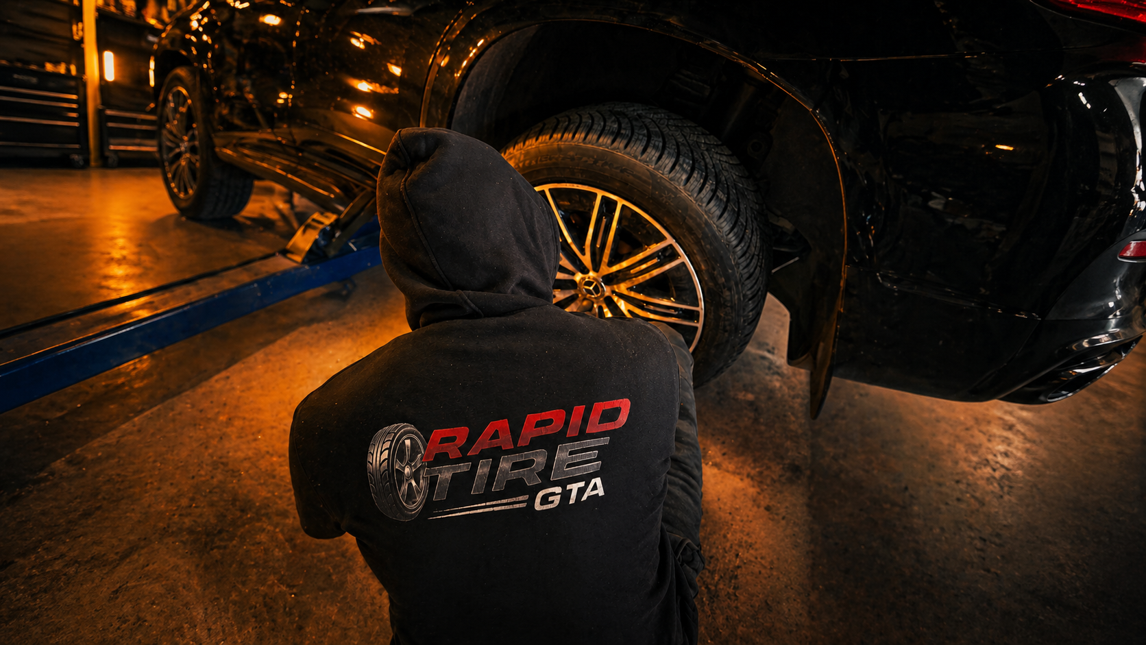 Roadside technician using professional impact wrench and hydraulic jack to replace a flat tire at night with amber warning lights